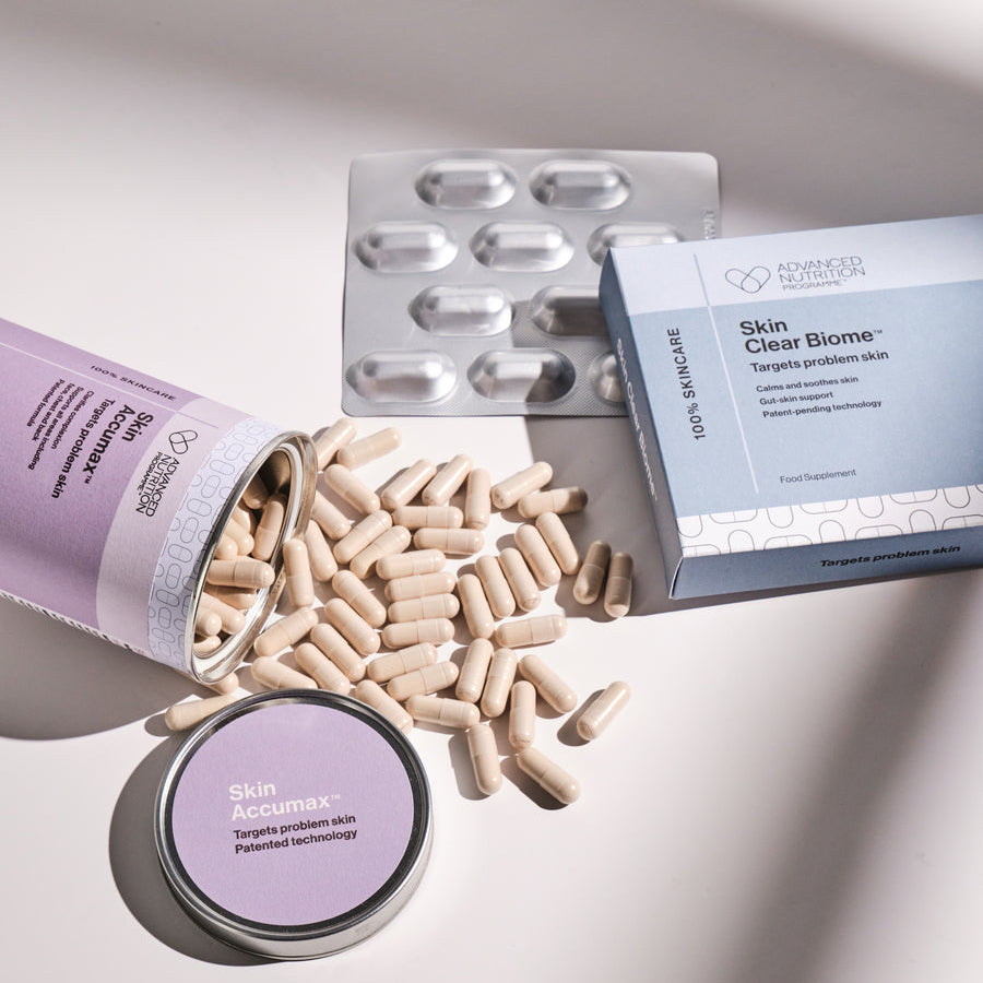 Supplement capsules spilling out of a container with a box labeled 'Skin Clear Biome' on a light gray background.